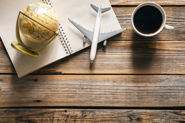 Erdkugel-Flugzeugmodell-Kaffeetasse und Notizblock auf Draufsicht des hölzernen Hintergrundes