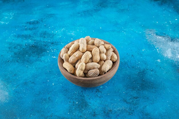 Erdnüsse in der Schale in einer Schüssel auf dem blauen Tisch.