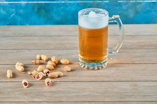 Erdnüsse und ein Glas Bier auf Holztisch.