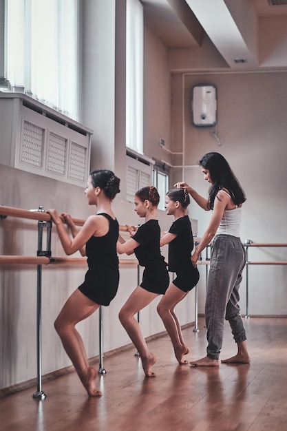 Erfahrene Ballettlehrerin zeigt jungen Ballerinas wichtige Übungen und korrigiert sie.