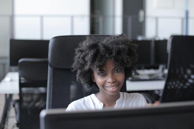 Erfolgreiche afroamerikanische Frau, die vor einem Computer sitzt, der in einem modernen Startup-Büro arbeitet