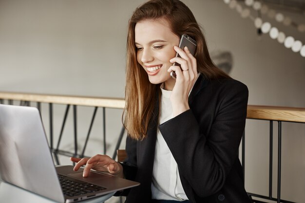 Erfolgreiche Geschäftsfrau, die lächelt, als sie am Telefon spricht und mit Laptop im Café arbeitet