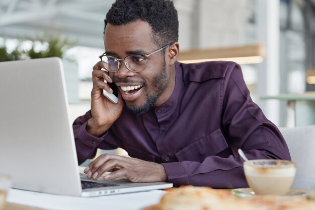 Erfolgreiche glückliche dunkelhäutige afrikanische männliche Führungskraft, lächelt glücklich und schaut auf Laptop-Computer