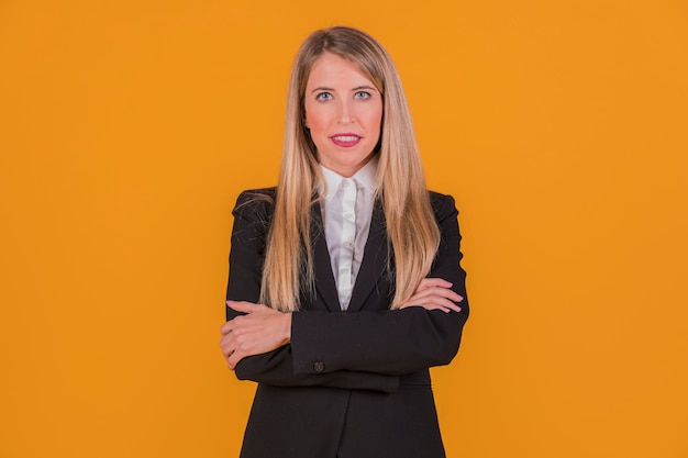 Erfolgreiche junge Geschäftsfrau, welche die Kamera steht gegen einen orange Hintergrund betrachtet