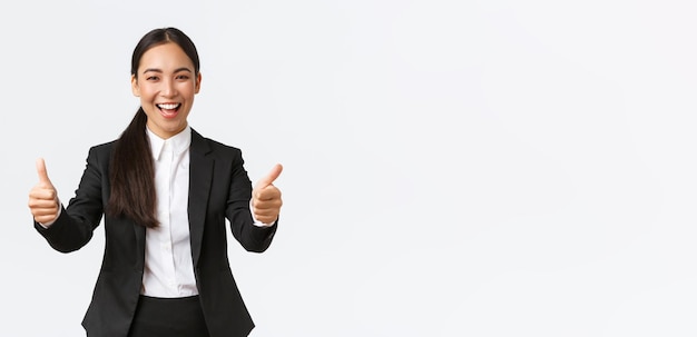 Erfolgreiche optimistische asiatische Geschäftsfrau, die Daumen hoch zeigt und fröhliche, fröhliche Managerin in Bu lächelt