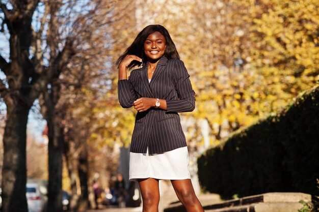 Erfolgreiche stylische afrikanisch-amerikanische Frau in Jacke und Rock posierte an einem sonnigen Herbsttag auf der Straße