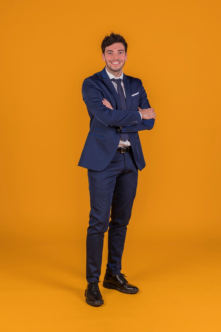 Kostenlose Foto erfolgreicher hübscher lächelnder junger mann mit seinem arm kreuzte stellung gegen einen orange hintergrund