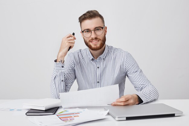 Erfolgreicher professioneller männlicher Unternehmer hält Papier und Stift, liest aufmerksam Vertrag