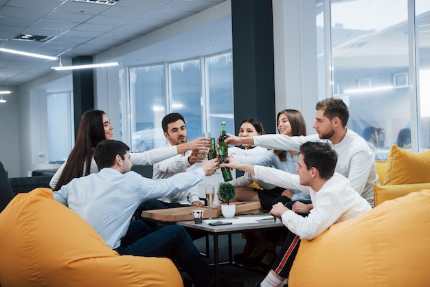 Erfolgreiches Geschäft feiern. Junge Büroangestellte sitzen in der Nähe des Tisches mit Alkohol