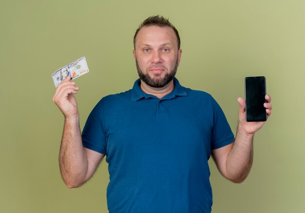 Erfreulicher erwachsener slawischer Mann, der Handy und Geld zeigt