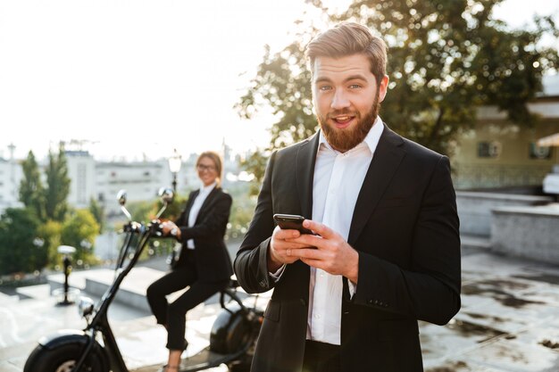 Erfreulicher Geschäftsmann, der draußen mit Telefon aufwirft