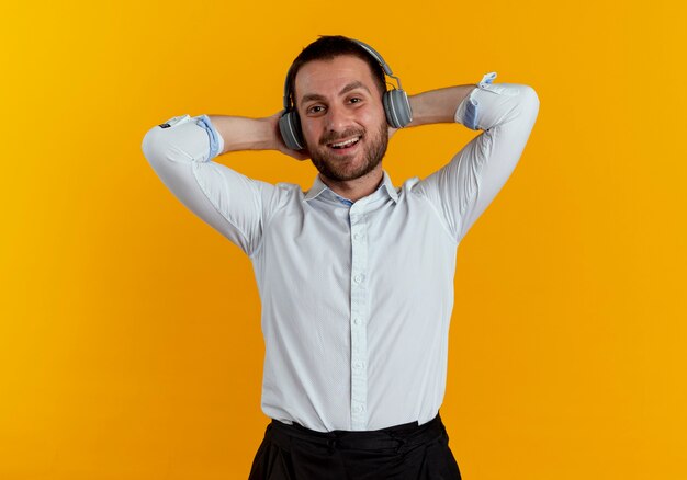 Erfreulicher gutaussehender Mann auf Kopfhörern hält Kopf hinter mit Händen, die auf orange Wand isoliert sind