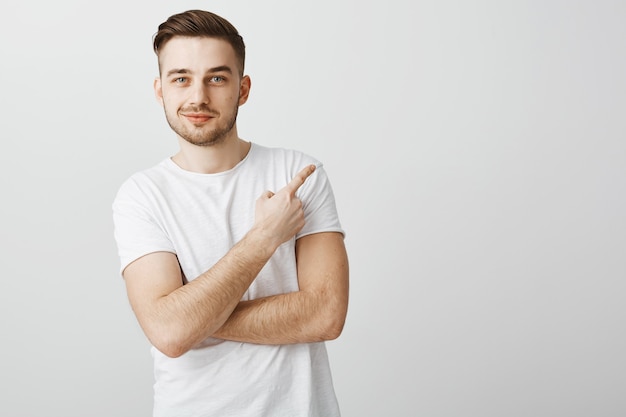 Erfreulicher hübscher junger mann im weißen t-shirt, der finger oben rechts zeigt