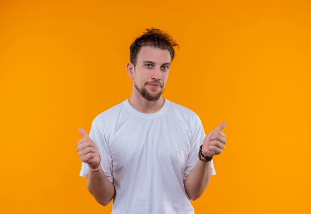 Erfreulicher junger Mann, der weißes T-Shirt seine Daumen oben auf lokalisiertem orange Hintergrund trägt