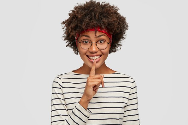 Erfreut emotionales dunkelhäutiges Mädchen zeigt Shush Geste