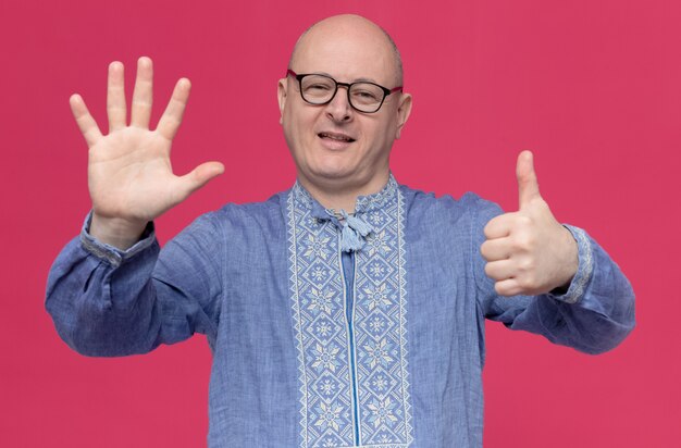 Erfreut erwachsener slawischer Mann im blauen Hemd mit optischer Brille, der sechs mit den Fingern gestikuliert