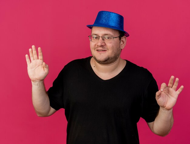 Erfreut erwachsener slawischer Mann in optischer Brille mit blauem Partyhut Gesten ok Handzeichen mit zwei Händen with