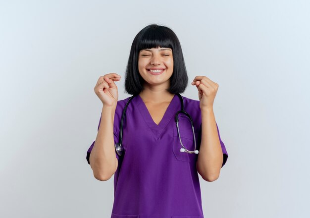 Erfreut junge brünette Ärztin in Uniform mit Stethoskop kreuzt die Finger