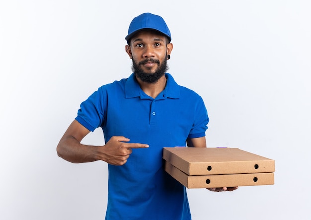 Erfreut junger afroamerikanischer Lieferbote, der Pizzakartons auf weißem Hintergrund mit Kopienraum isoliert hält und zeigt