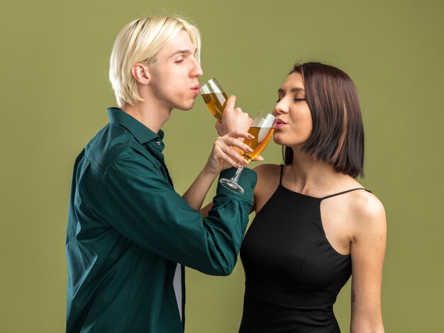 Erfreut junges Paar am Valentinstag trinkt ein Glas Champagner mit verschränkten Armen isoliert auf olivgrüner Wand