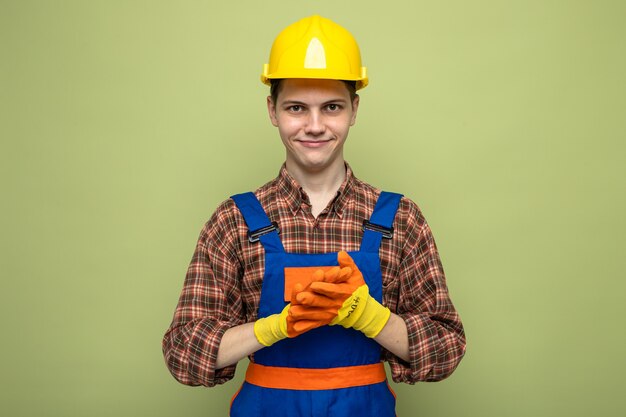 Erfreut mit den Händen zusammen junger männlicher Baumeister, der Uniform mit Handschuhen trägt