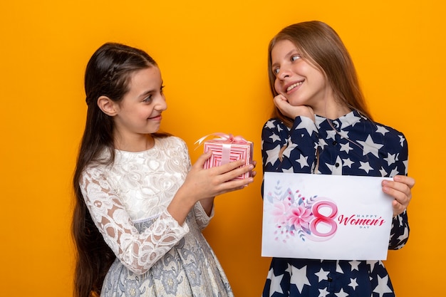 Erfreut, sich zwei kleine Mädchen am glücklichen Frauentag anzusehen, die Geschenk mit Grußkarte halten