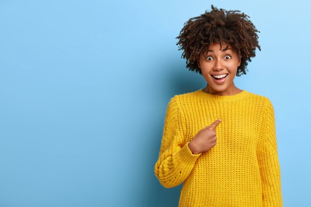 Erfreut überraschte Frau mit einem Afro, der in einem rosa Pullover posiert