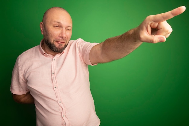 Kostenloses Foto erfreut, wenn man einen kahlen mann mittleren alters betrachtet, der rosa t-shirt-punkte an der seite trägt, die auf grün lokalisiert wird