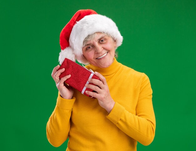 Erfreute ältere Frau mit Weihnachtsmütze hält Weihnachtsgeschenkbox