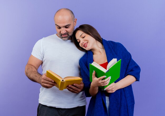 Erfreute erwachsene Paarfrau in Schal gewickelt, Buch haltend und Blick auf die Buchfrau des Mannes, die den Kopf auf seine Schulter legt