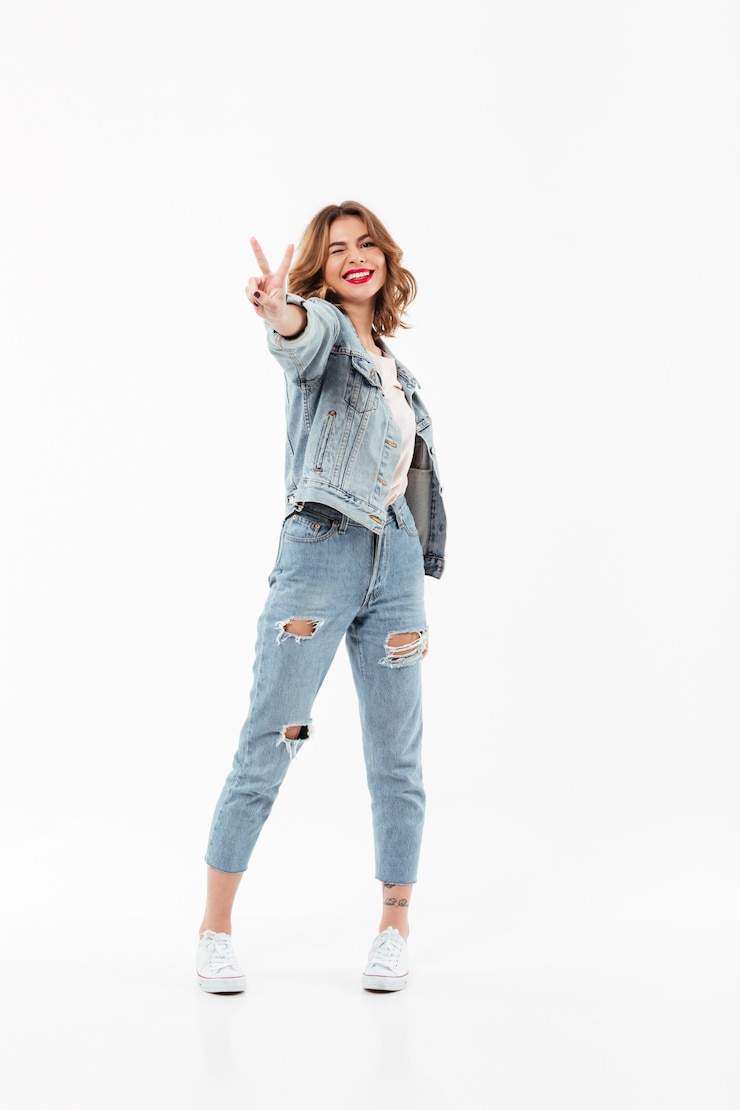 Kostenlose Foto erfreute frau in voller länge in der denimkleidung blinzelt und friedensgeste über weißer wand zeigend