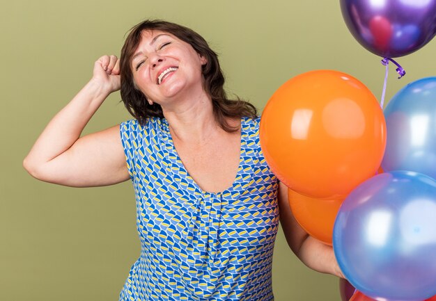 Erfreute Frau mittleren Alters mit einem Haufen bunter Ballons, die glücklich und aufgeregt die Faust heben