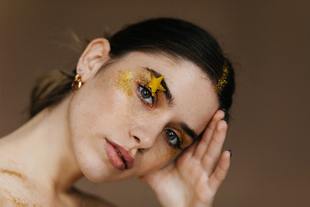 Erfreute junge Dame mit glamourösem Make-up. Positives brünettes Mädchen, das ihre Stirn berührt.