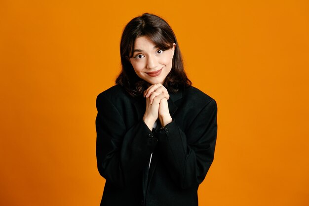 erfreute junge schöne Frau mit schwarzer Jacke isoliert auf orangefarbenem Hintergrund