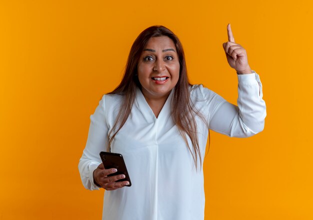 Erfreute zufällige kaukasische Frau mittleren Alters, die Telefon hält und nach oben zeigt