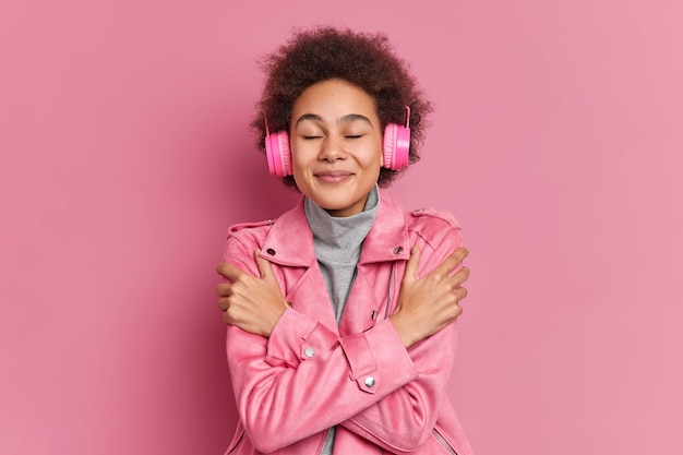 Kostenloses Foto erfreutes gut aussehendes mädchen mit lockigem afro-haar schließt die augen, umarmt sich und hört musik