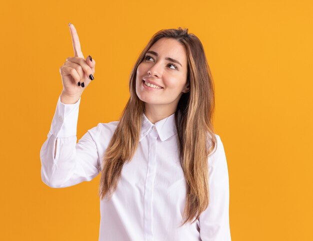 Erfreutes junges hübsches kaukasisches Mädchen schaut und zeigt auf Orange