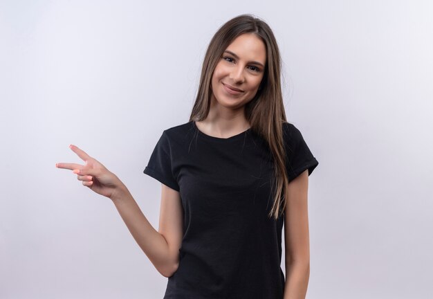 Erfreutes junges kaukasisches Mädchen, das schwarzes T-Shirt trägt, das Friedensgeste auf lokalem weißem Hintergrund zeigt