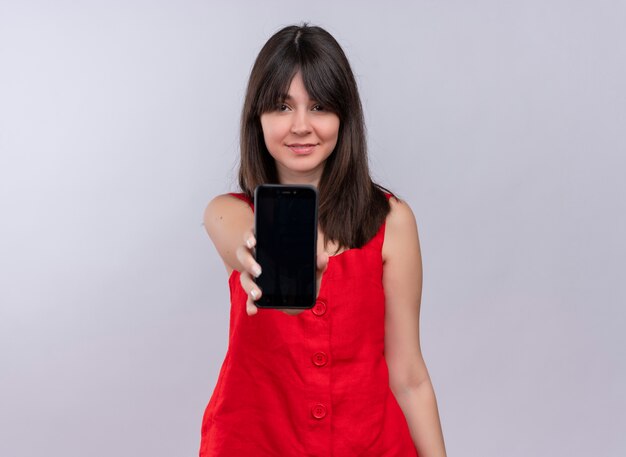 Erfreutes junges kaukasisches Mädchen, das Telefon gerade hält und Kamera auf lokalisiertem weißem Hintergrund betrachtet