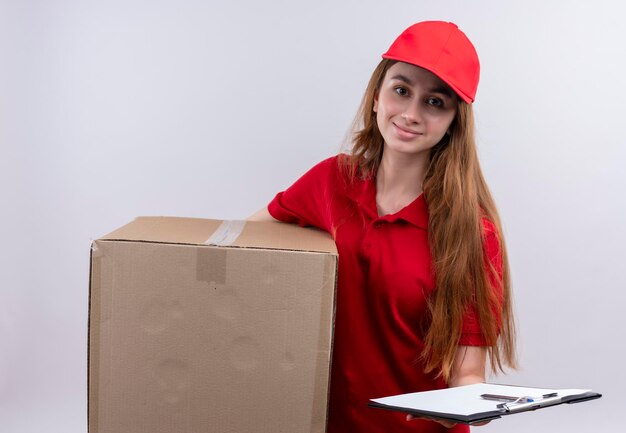 Erfreutes junges Liefermädchen in der roten Uniform, die Box und Zwischenablage auf lokalisiertem weißem Raum hält