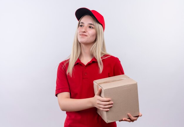 Erfreutes junges Mädchen der Lieferung, das rotes T-Shirt und Kappenhaltebox auf lokalem weißem Hintergrund trägt