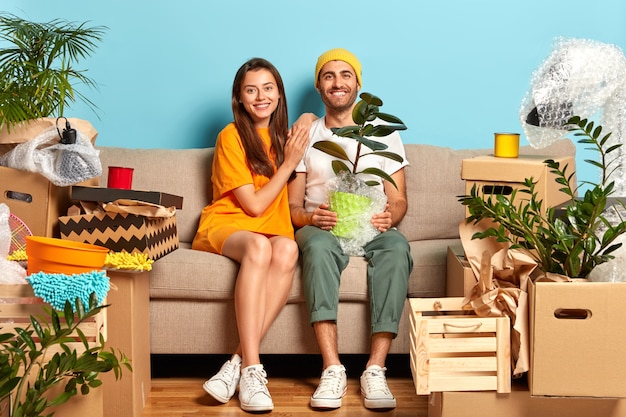 Erfreutes junges Paar sitzt auf der Couch, umgeben von Kisten