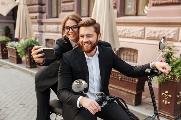 Erfreutes stilvolles Paar, das draußen auf modernem Motorrad sitzt
