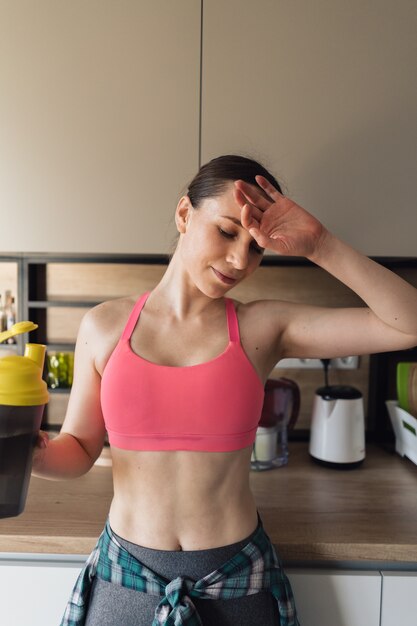 Erfreutes Trinkwasser der Frau nach dem Training zu Hause