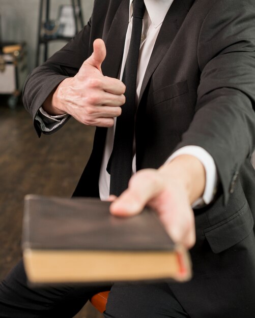 Erfüllter Geschäftsmann, der das Buch sich zeigt Daumen zeigt