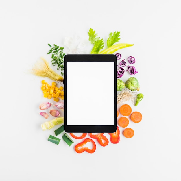 Erhöhte Ansicht der digitalen Tablette auf verschiedenem Gemüse über weißem Hintergrund