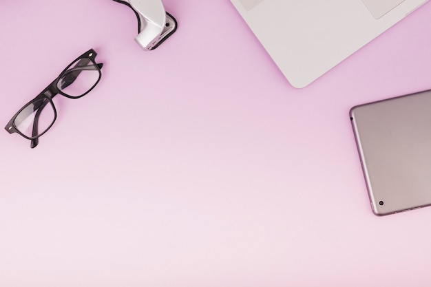 Erhöhte Ansicht der digitalen Tablette; Brille und Laptop auf rosa Hintergrund