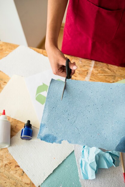 Erhöhte Ansicht der Hand der Frau blaues Papier mit Scheren schneiden