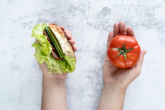 Erhöhte Ansicht der Hand der Person Tomate und Burger über konkretem Hintergrund in der Hand halten