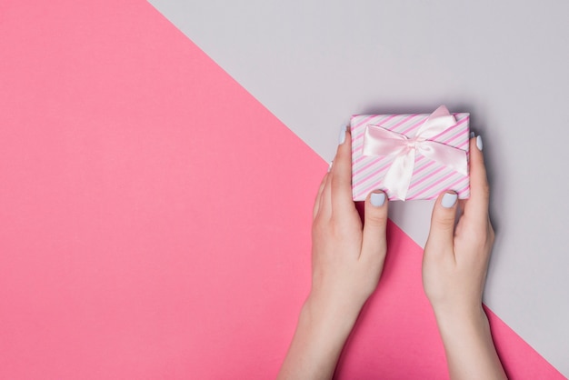 Erhöhte Ansicht der Hand Geschenkbox gegen doppelten rosa und grauen Hintergrund halten